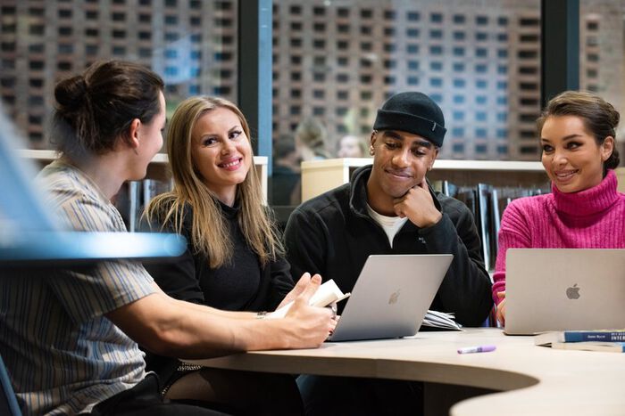 Bildet inneholder smil, datamaskin, flere studenter rundt et bord