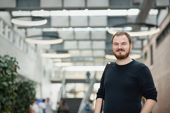 Mannlig student med skjegg står oppreist og smiler, vrimlehallen