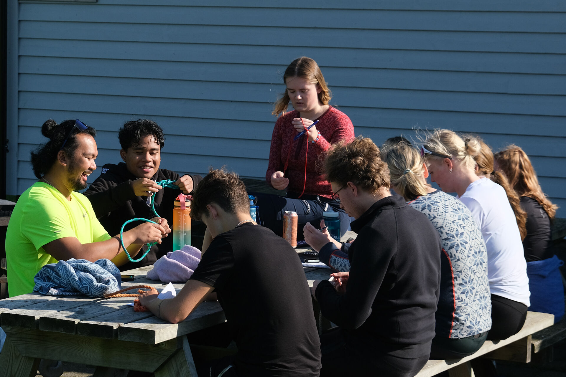 Gruppe studenter sitter rundt på en piknikbenk øver på knuter