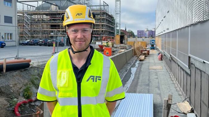 Portrett av en mann med gul refleksvest og vernehjelm på en byggeplass.