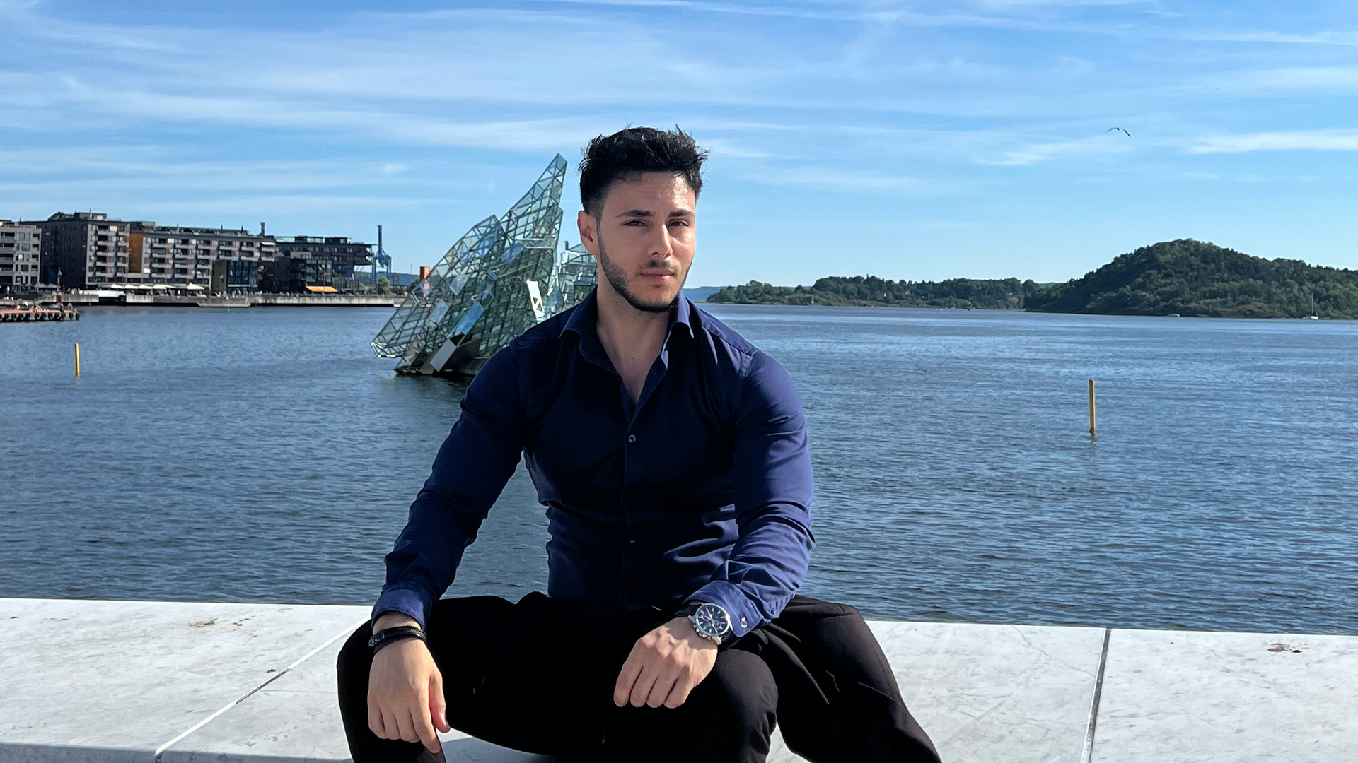 Adam sitter foran oslofjorden og ser inn i kamera
