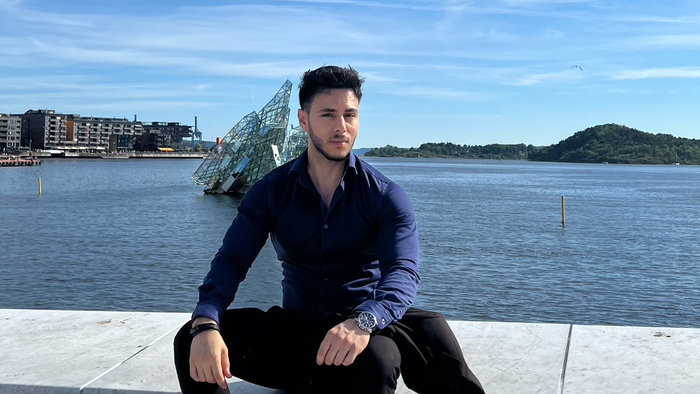 Adam sitter foran oslofjorden og ser inn i kamera 