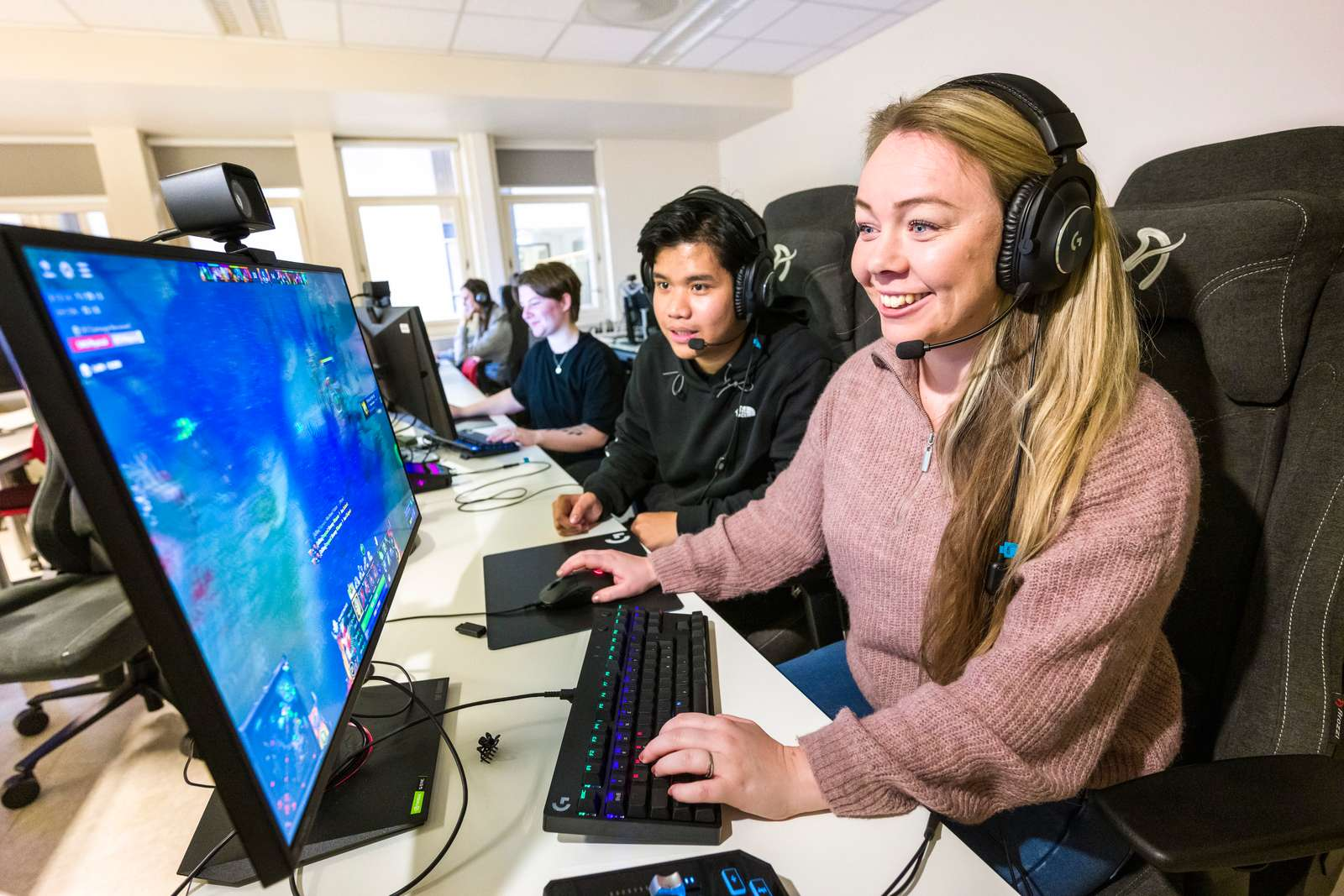 Voksen person og ungdom sitter foran PC med hodetelefoner og spiller dataspill