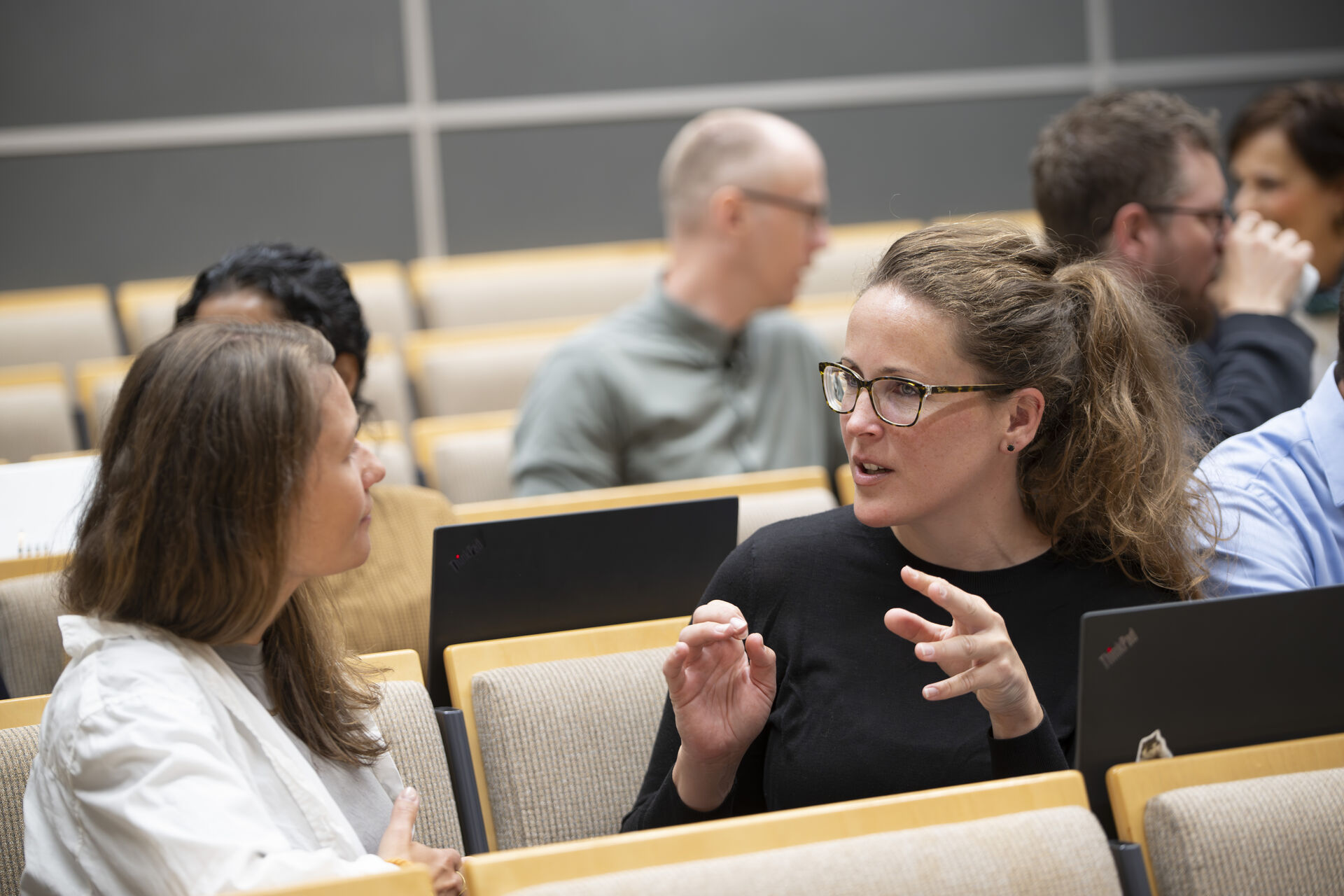 to kvinner i dialog i et auditorium med andre studenter