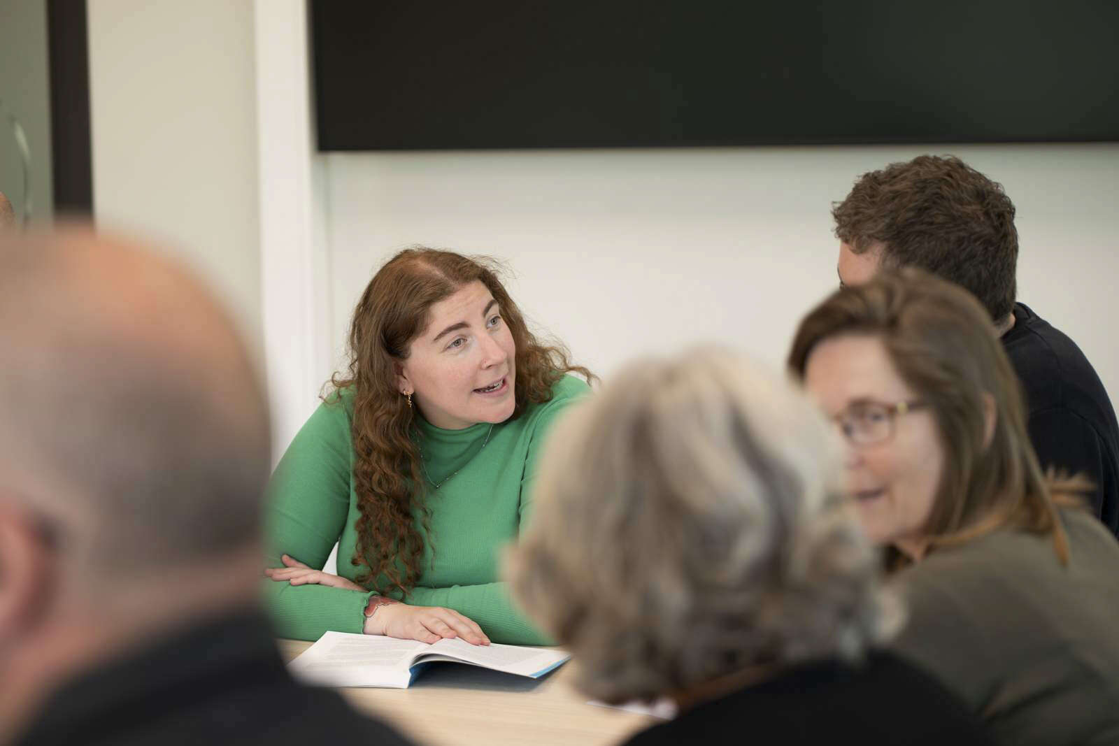 Kvinne forklarer noe i et klasserom med to medstudenter rundt seg