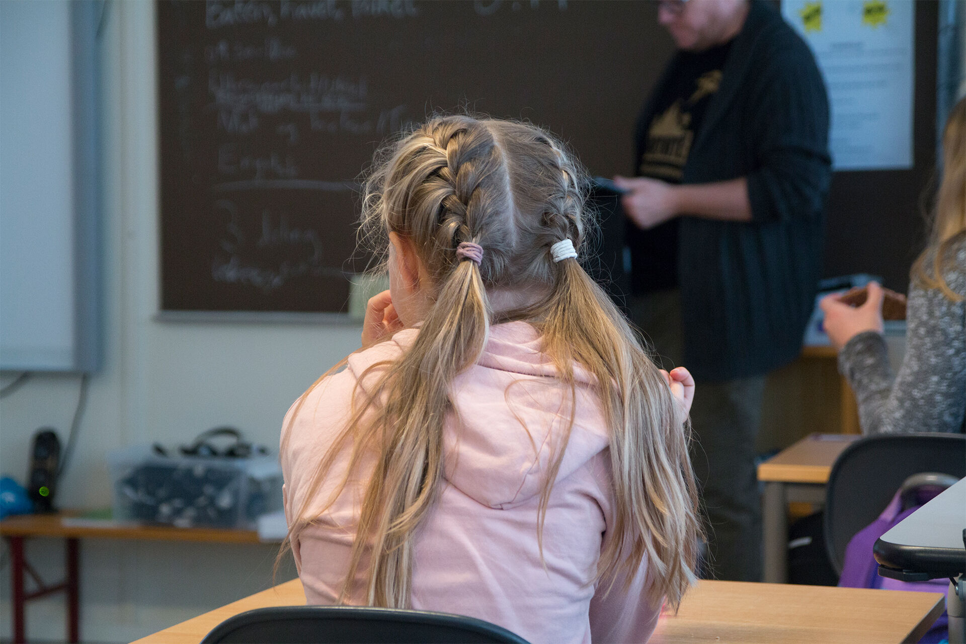 En jente sitter og hører på lærere snakke i et klasserom