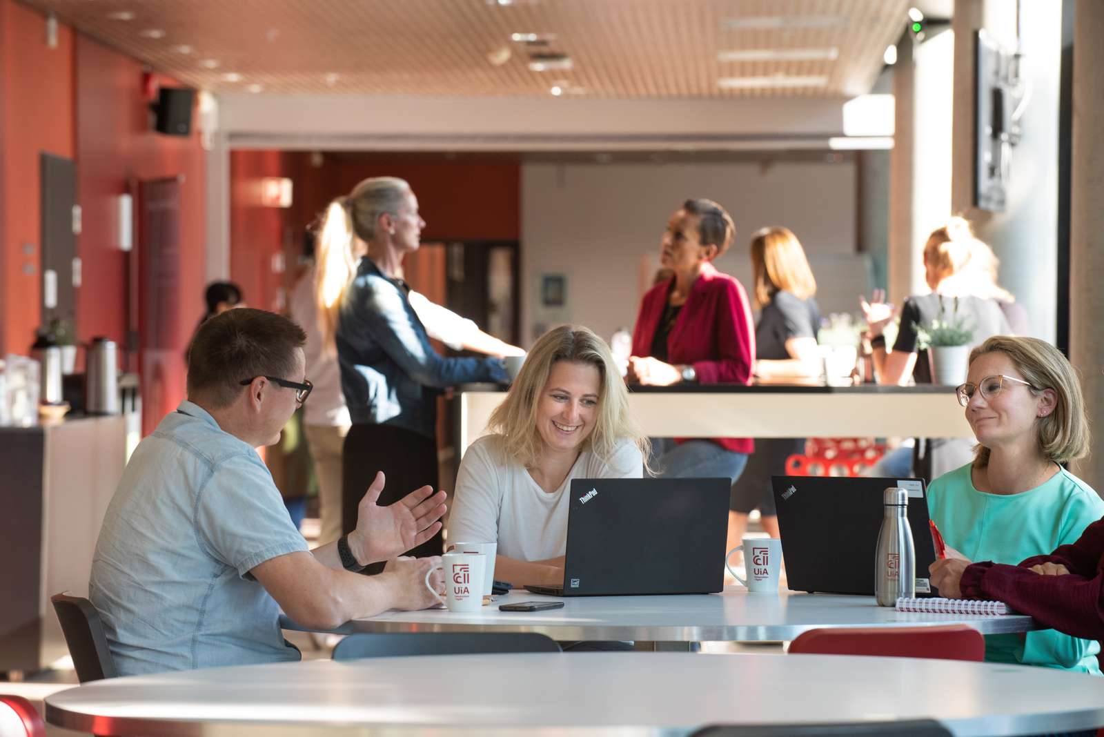 Tre studenter som sitter ved et bord og studerer og diskuterer