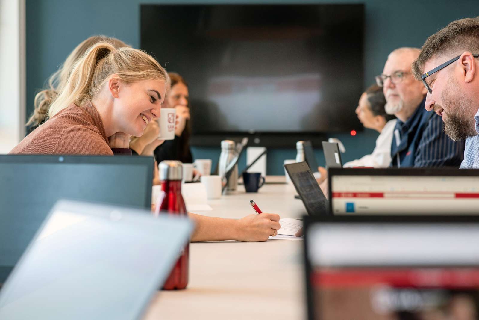 Smilende kvinne med penn i hånden skriver noe på et papir og viser til mannlig medstudent