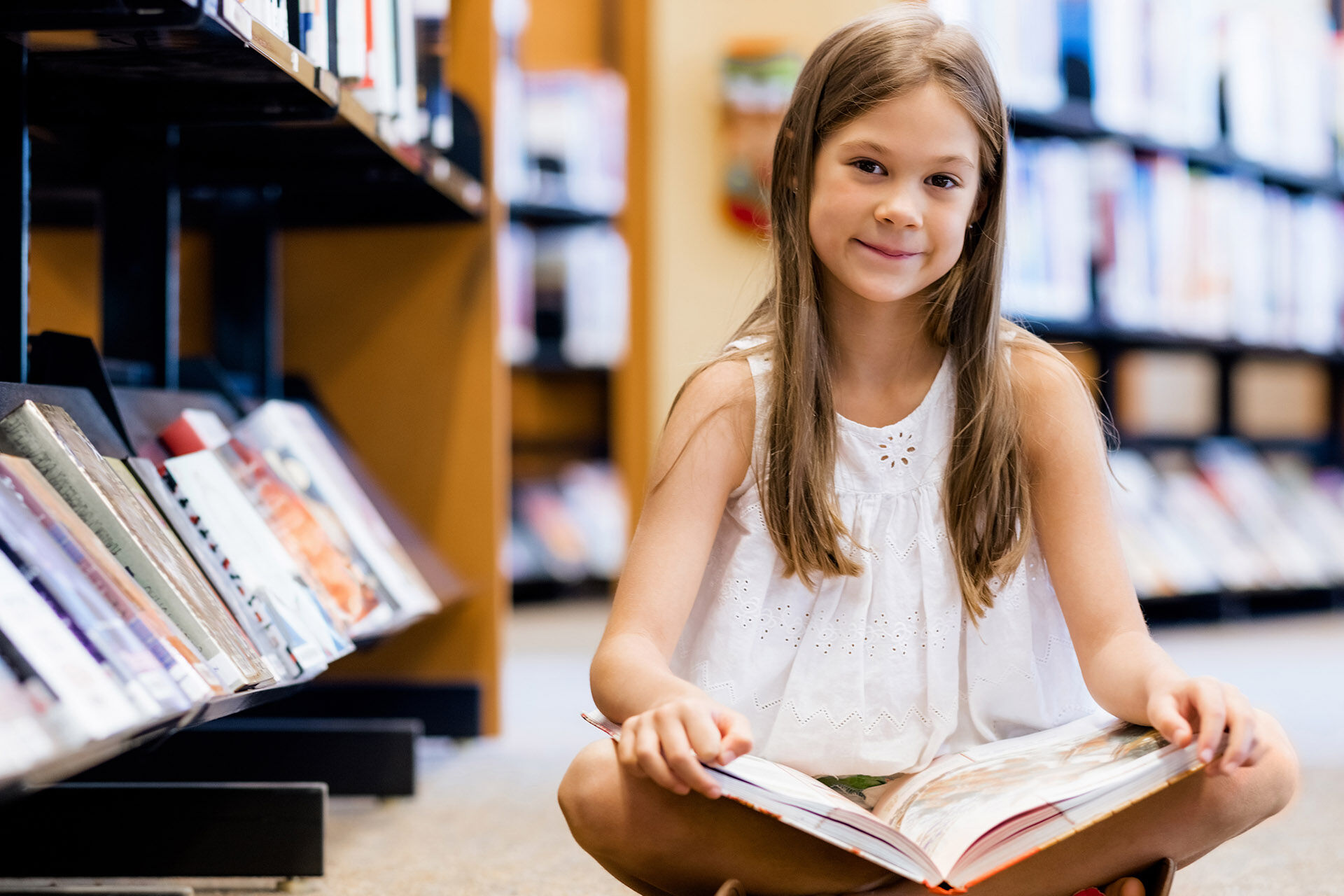 En jente sitter på gulvet i et bibliotek og leser i en bok