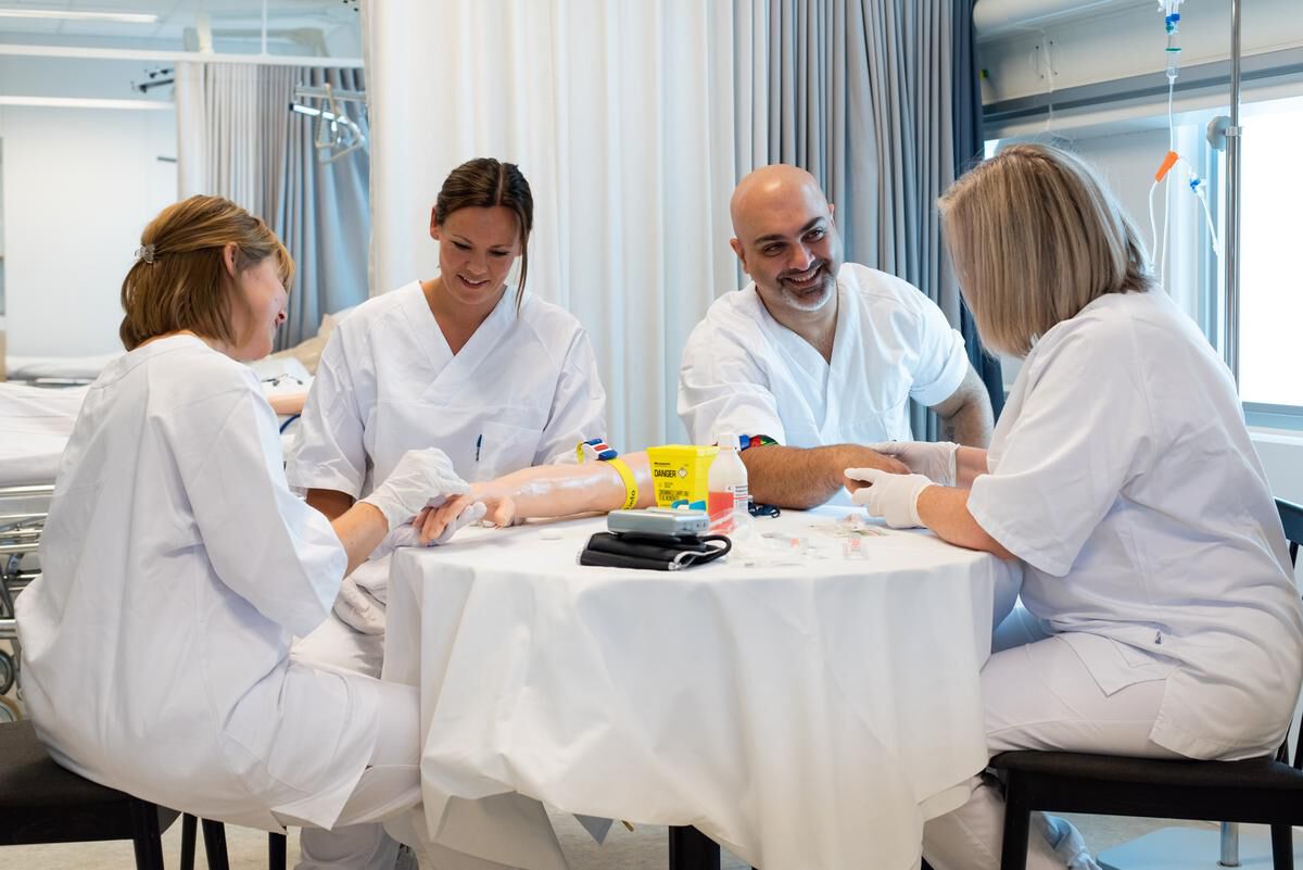 Tre kvinner og en mann sitter i hvit helseuniform rundt et bord