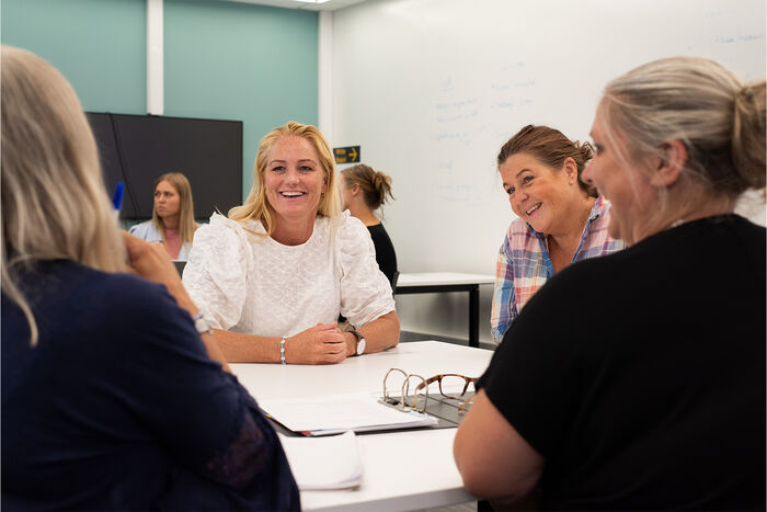 gruppe på fire som sitter rundt et bord i undervisning. Samtale, smil.
