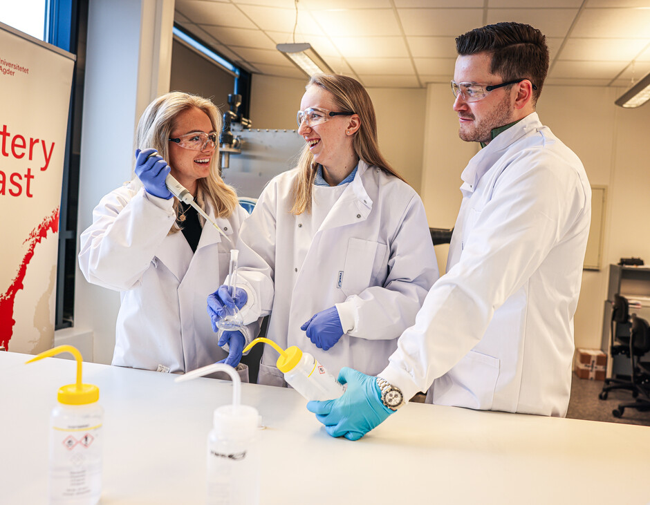 Tre studenter i labfrakk, vernebriller og plasthandsker står på labben og renser glass til studier i batterielektrolytter