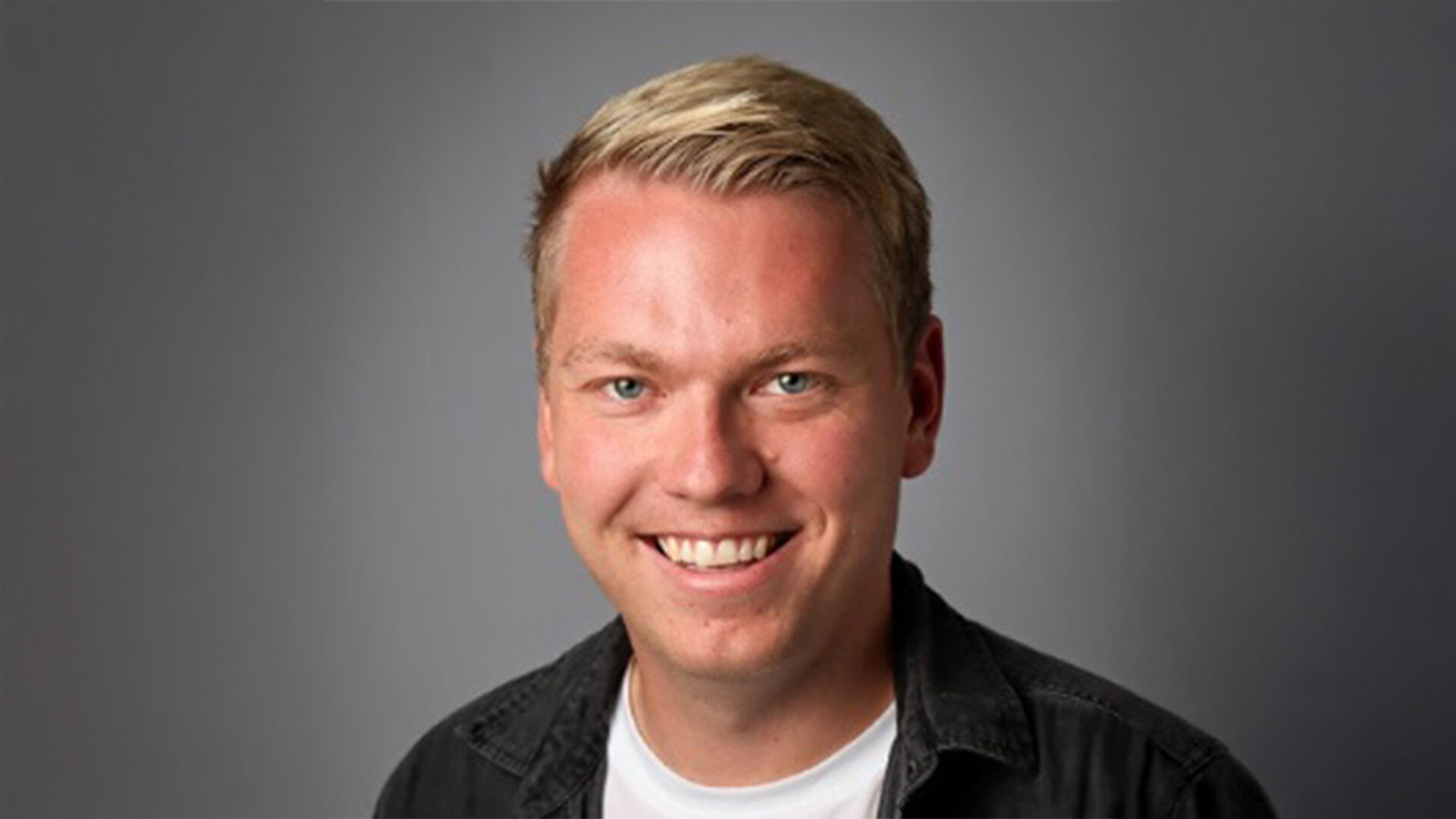 Portrettfoto av Kristoffer Ask foran en vegg med Stormberg-logo