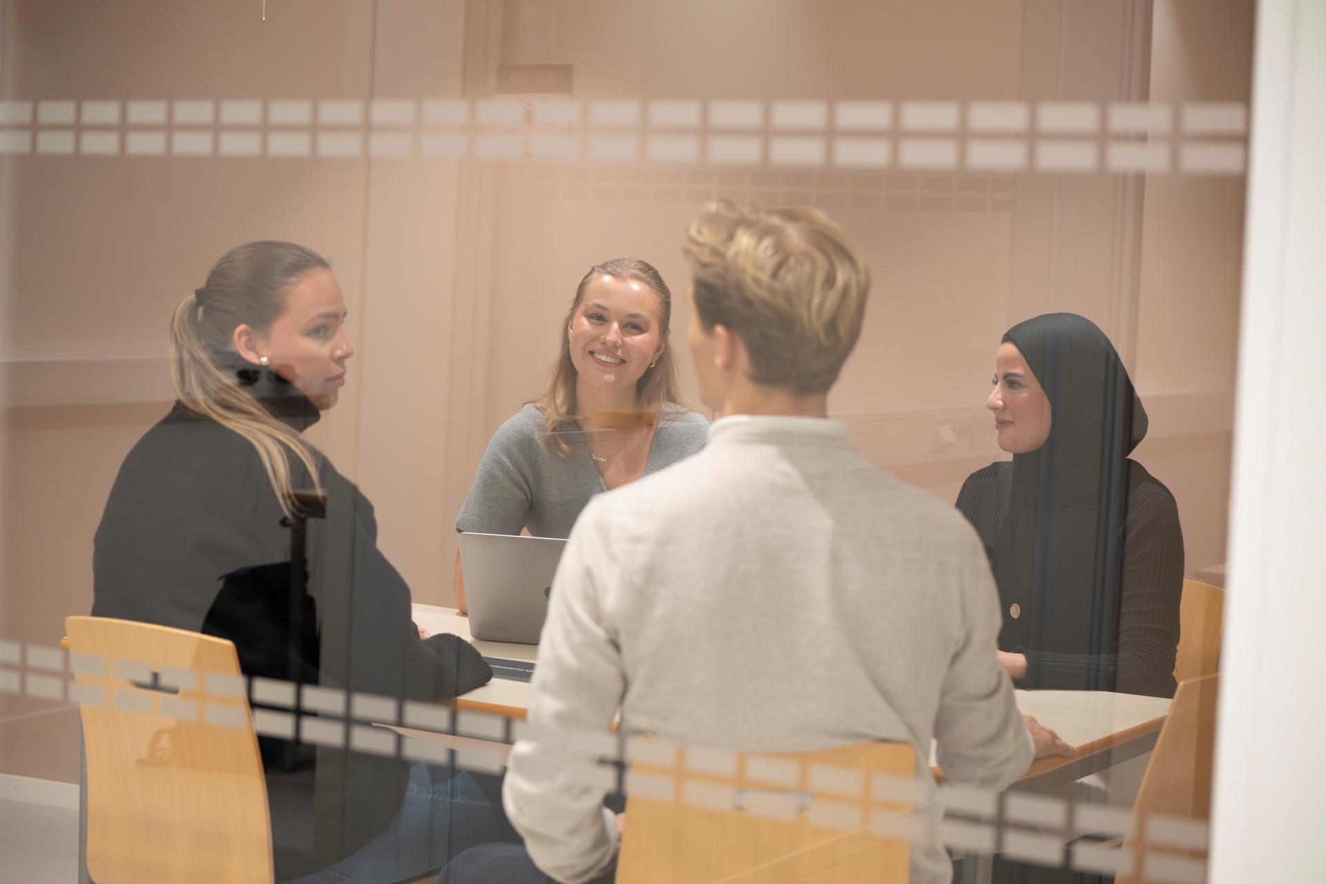 Bilde av fire studenter som jobber sammen i et grupperom sett gjennom en glassvegg