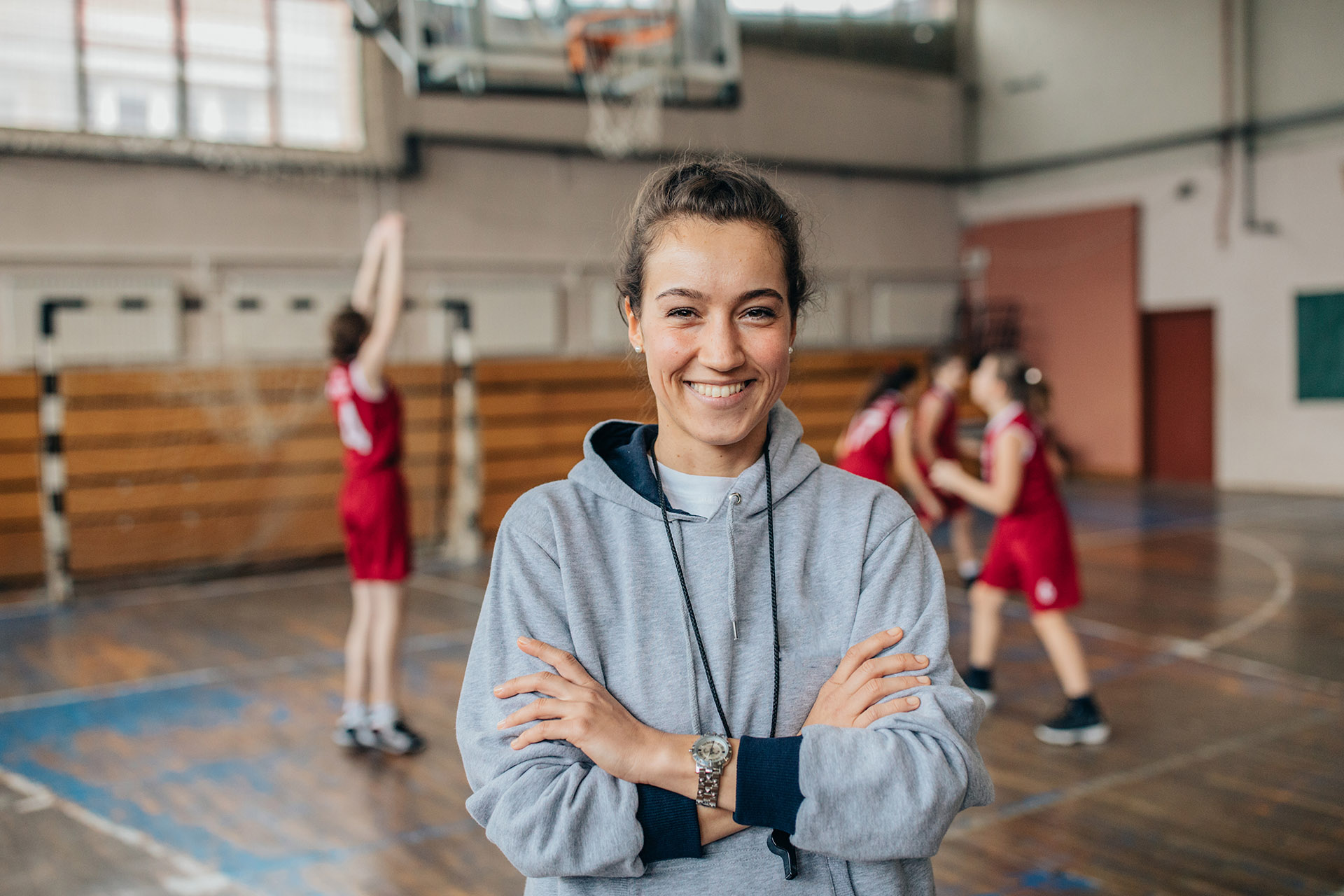 Bilde av en smilende student i en idrettshall foran noen som spiller basketball