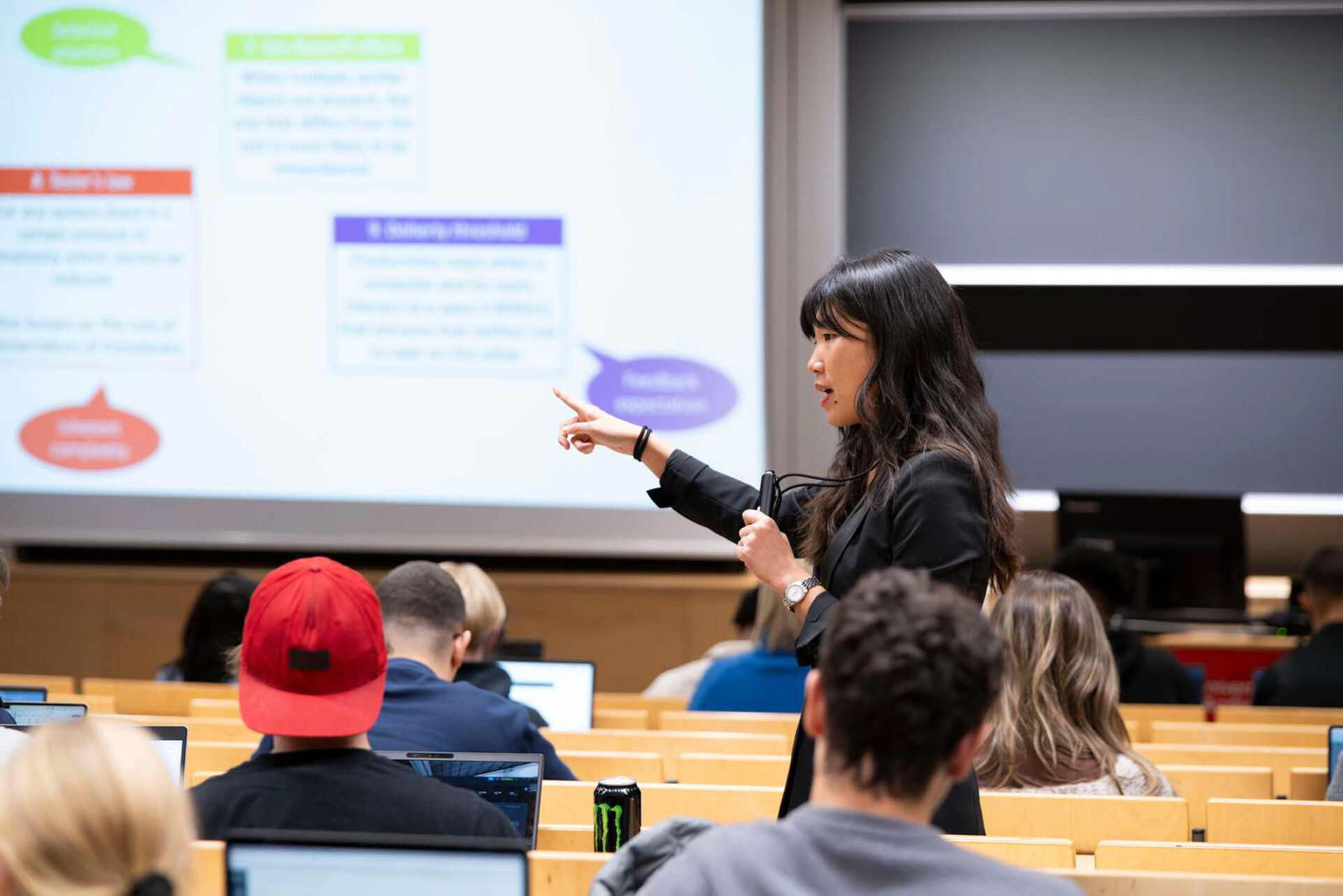 Foreleser peker mot presentasjonen sin og forklarer til studenter i salen.