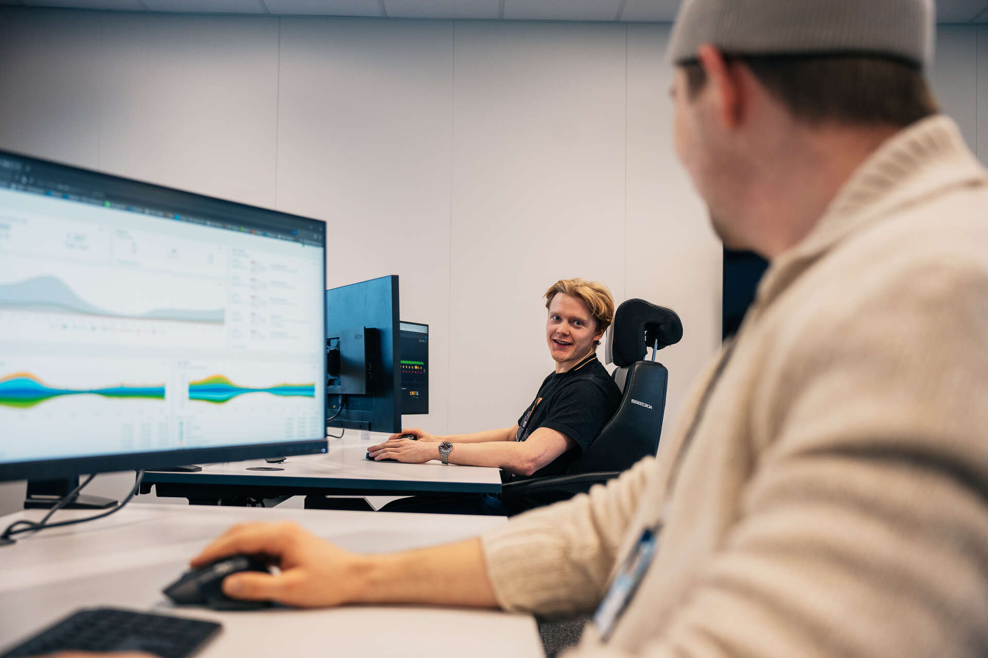 Bilde hvor en ser hendene til en som jobber foran PC-skjermer med koder