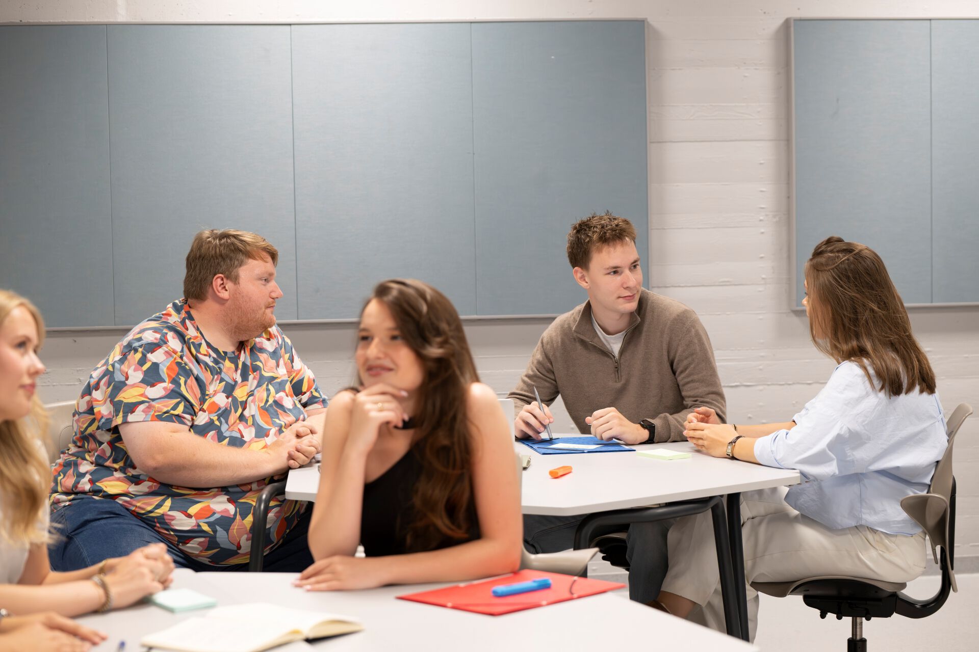 Bilde av studenter i et klasserom som sitter rundt bord og snakker sammen