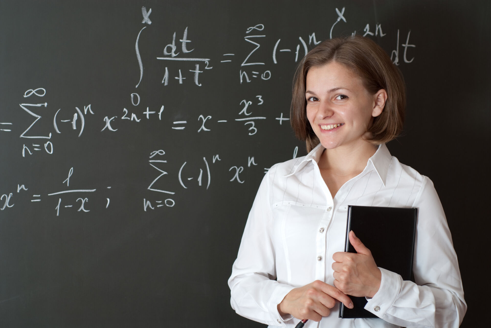 Smilende kvinne som står foran en tavle med matematiske tegn