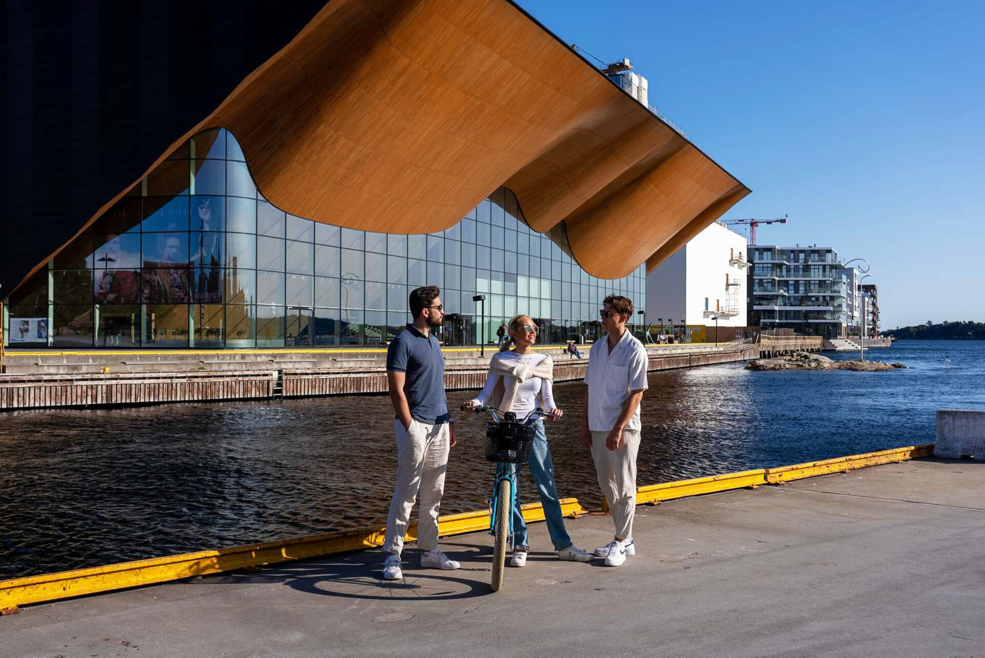 Tre studenter står og snakker sammen foran Kilden kulturhus, en med sykkel