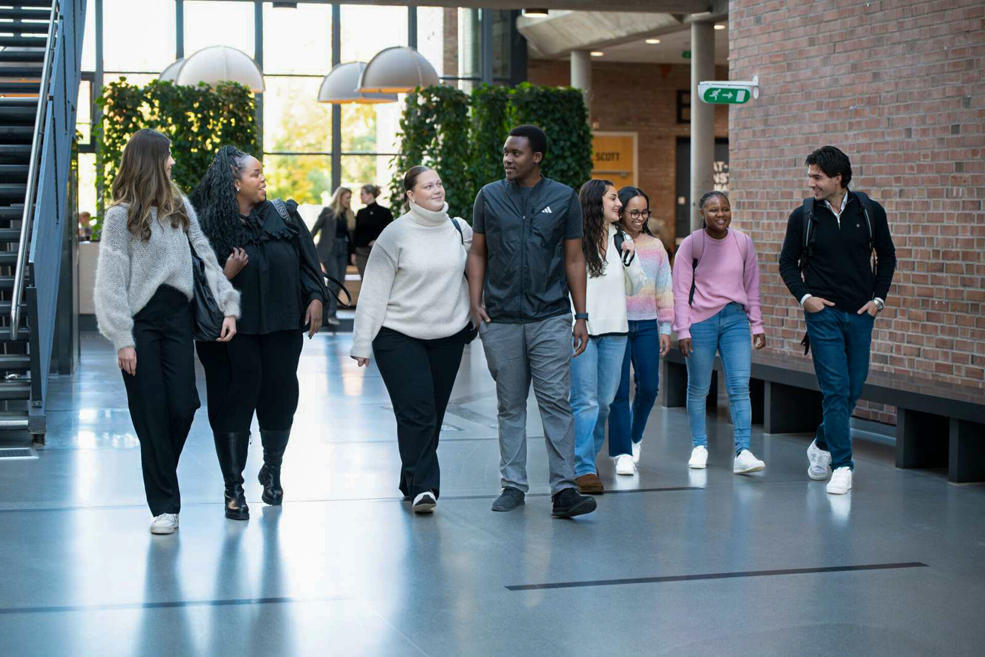 Åtte studenter kommer gående i en aula, ser på hverandre og snakker sammen