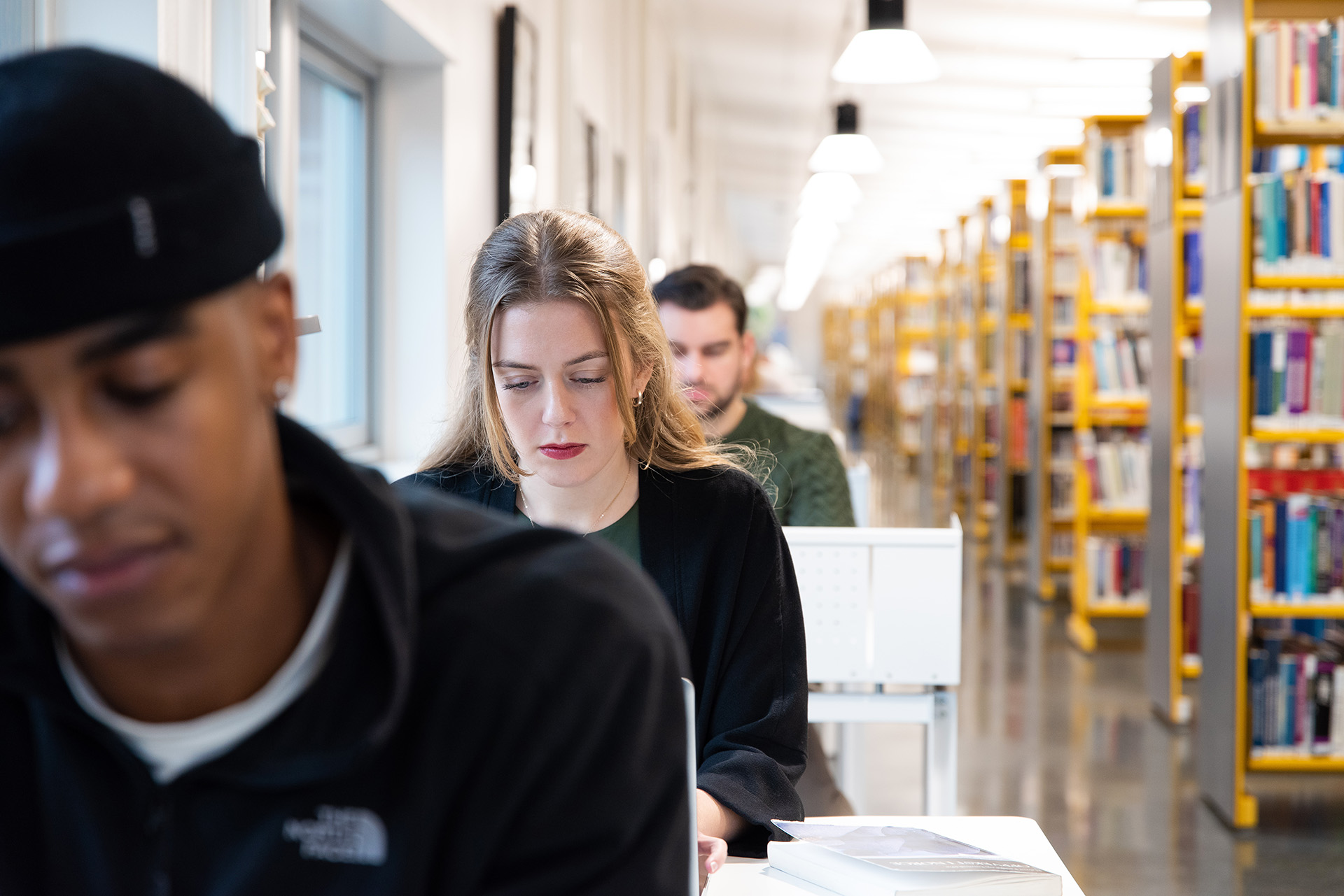 Studenter sitter i dyp konsentrasjon, på en rekke av skrivebord, i et bibliotek.