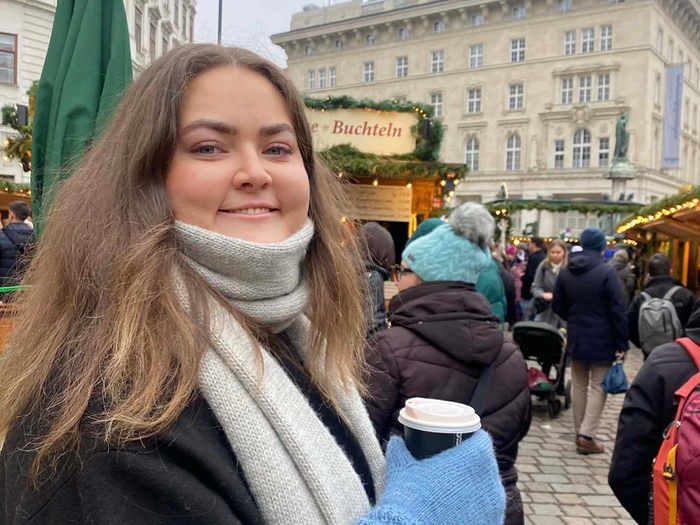 Marianne står ute i byen, holder en kaffekopp og smiler til kamera