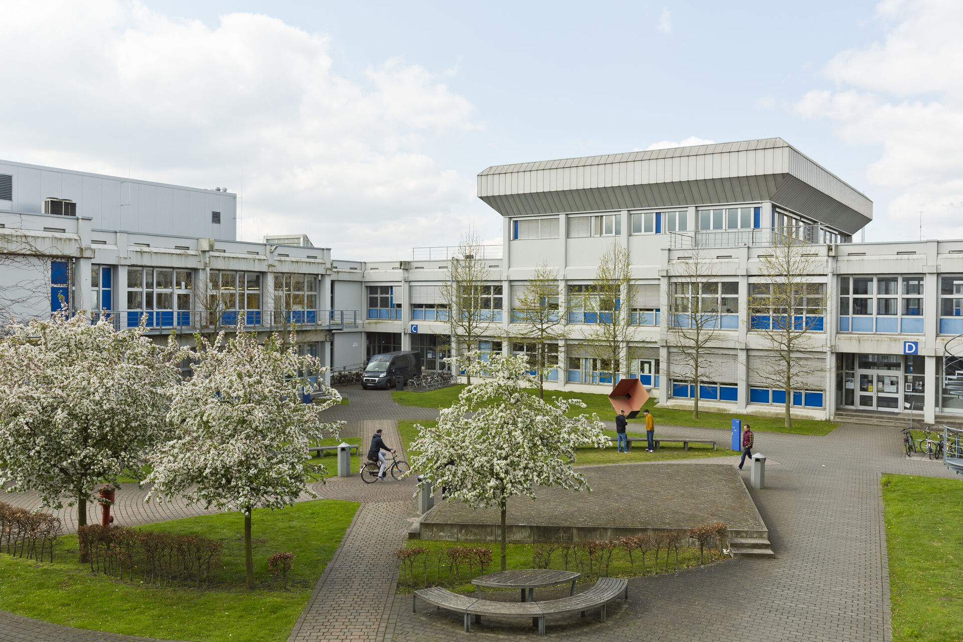 Bildet viser deler av campus til universitetet, med trær i forgrunnen og person som går rundt