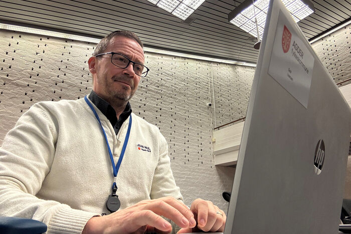 Mann med briller sitter og ser på en pc. 