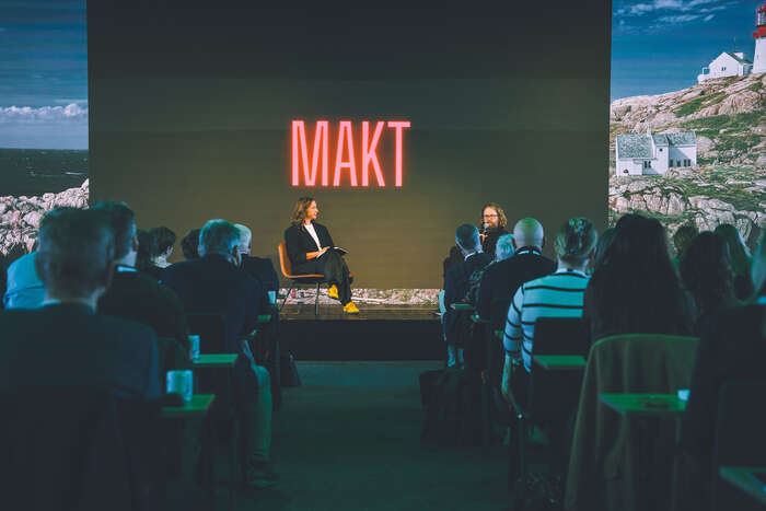 En mann og en kvinne sitter på en scene og snakker foran et publikum.