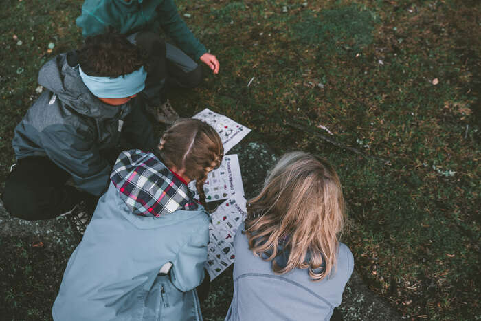 Tre barn er ute og løser en naturquiz gjennom uteskole