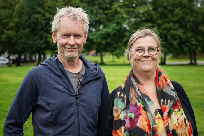 En mann med grått hår og blå jakke og kvinne med langt hår og briller smiler inn i kamera.