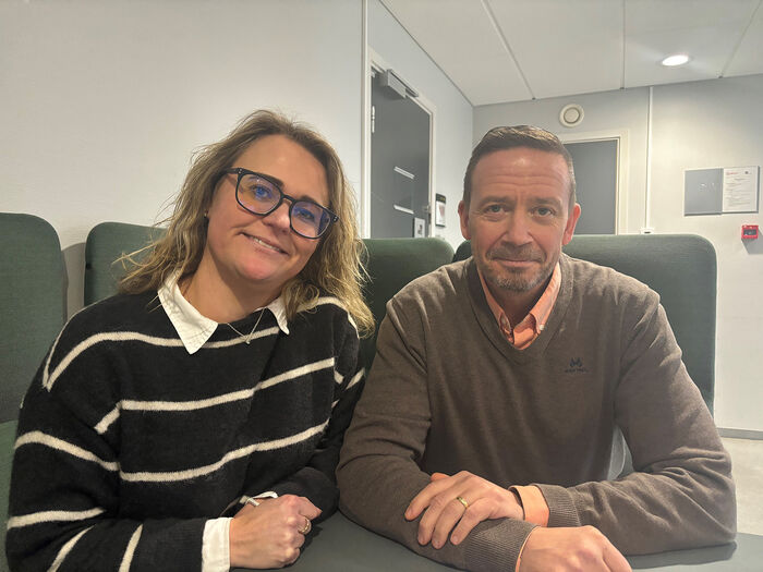 En kvinne med briller i stripete genser sitter til venstre for en mann som smiler. 