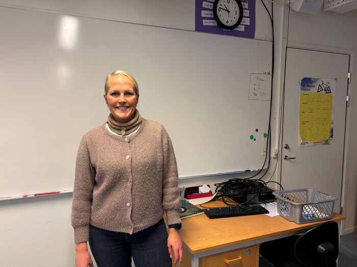 Smilende kvinne står foran en tavle på en skole.