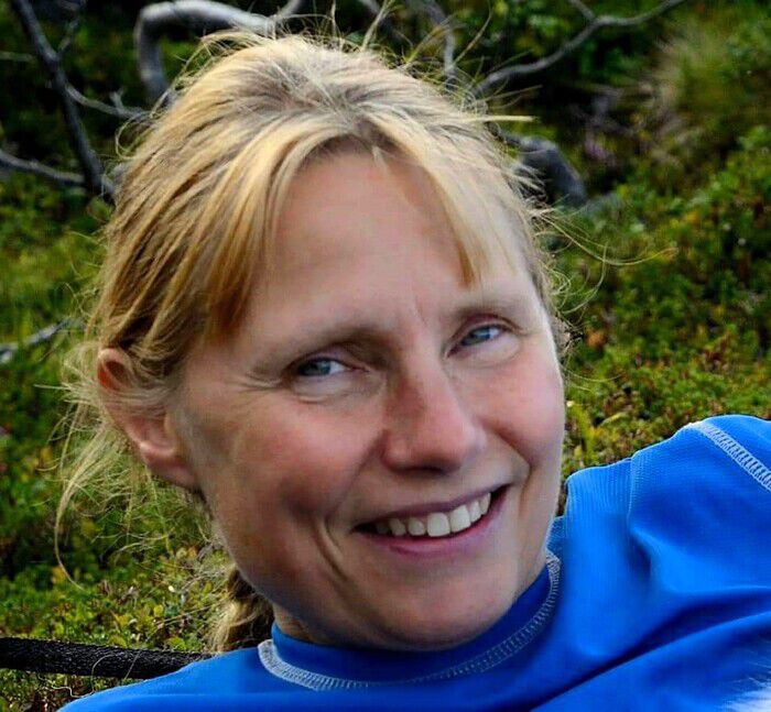 Kvinne med lyst hår og blå genser smiler inn i kamera