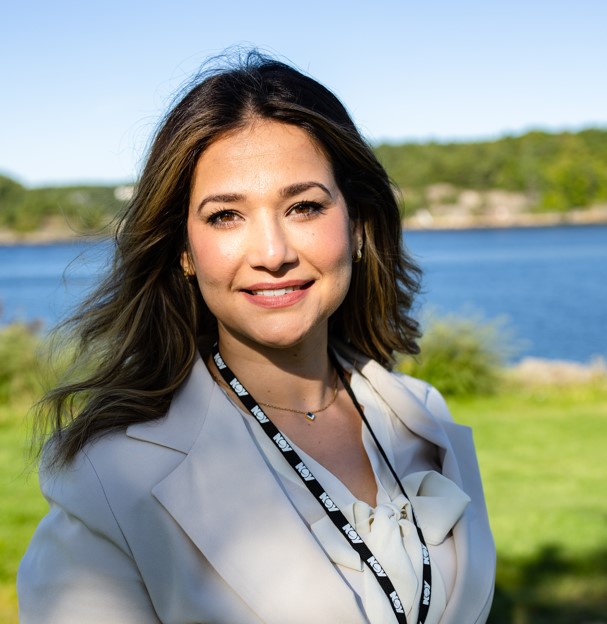 Kvinne i hvit dress, med mørkt hår og mørke øyne, smiler
