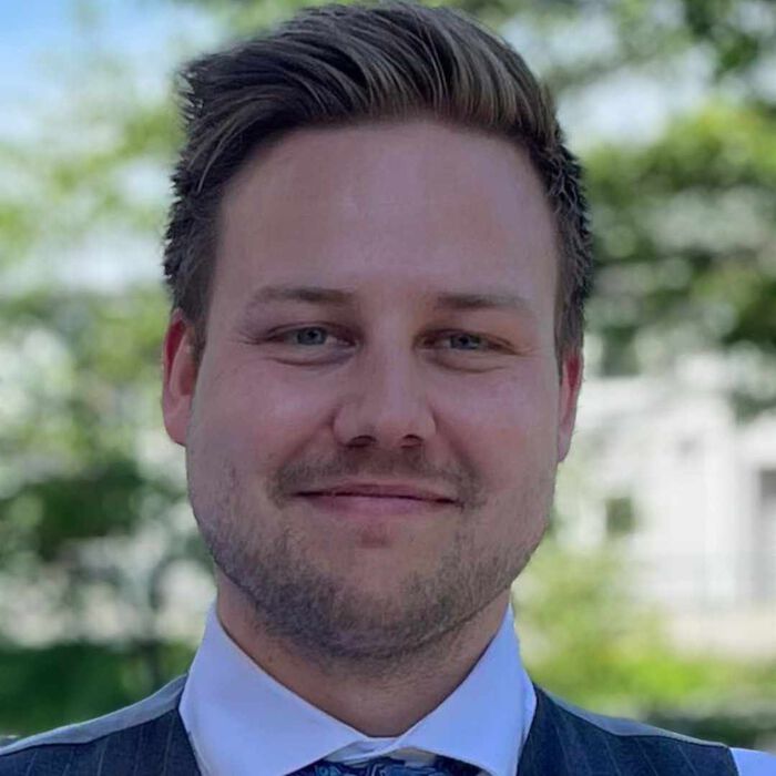 En mann med tredagers skjegg og kort hår smiler inn i kameraet