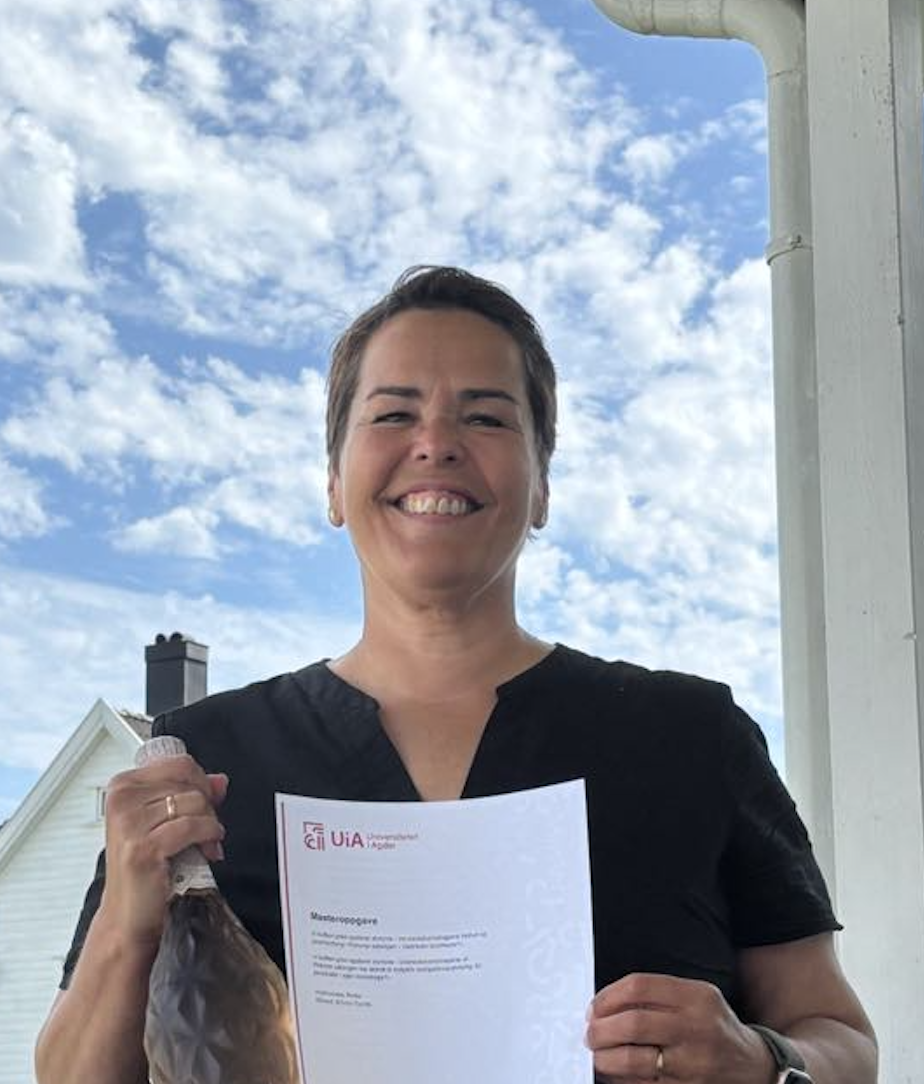 Smilende kvinne med kort mørkt hår ser rett inn kamera mens hun holder en sjampanjeflaske og et master diploma i hendene.